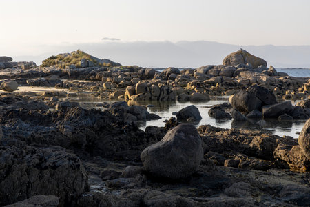 A rocky beach with a large rock in the foreground. The beach is empty and the sky is cloudy.の写真素材