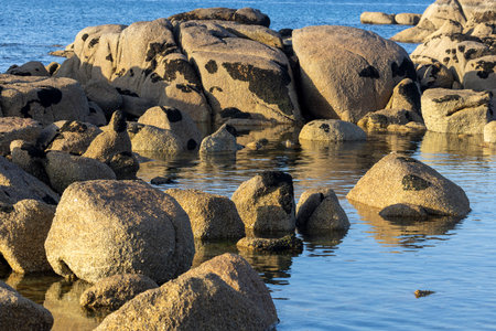 A rocky shoreline with a body of water in the background. The water is calm and the rocks are scattered throughout the sceneの写真素材