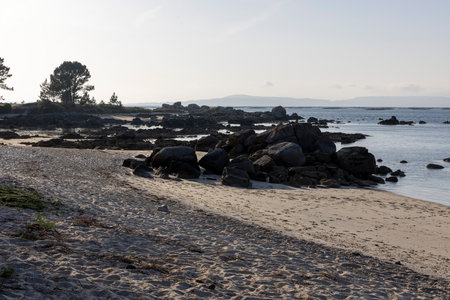 A rocky beach with a large rock in the foreground. The ocean is calm and the sky is clearの写真素材