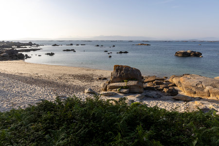 A rocky beach with a large rock in the foreground. The ocean is calm and the sky is clearの写真素材
