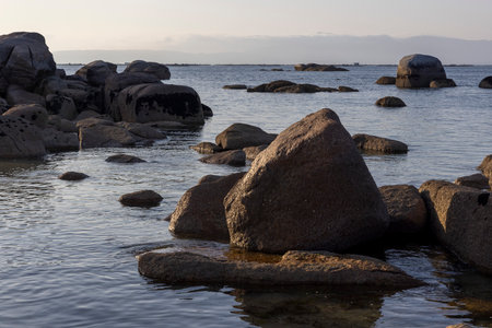 A large rock sits in the middle of a body of water. The water is calm and the sky is clear. The rock is surrounded by rocks and the scene is peacefulの写真素材