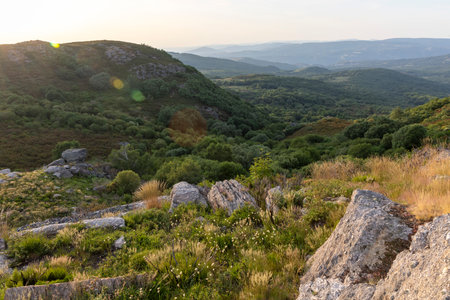 A mountain range with a lush green valley below. The sky is a mix of blue and white, with a few clouds scattered. The scene is peaceful and serene, with the mountainsの写真素材