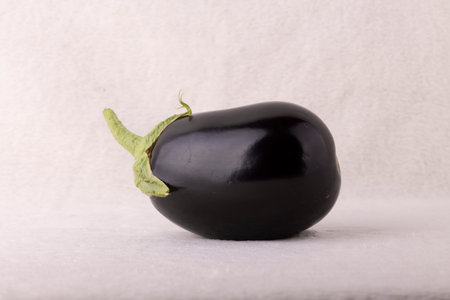 A black eggplant with a green stem is sitting on a white background. The eggplant is the main focus of the image, and it is the only object in the sceneの写真素材