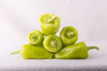 A bunch of green peppers are piled on top of each other. The peppers are all different sizes and are arranged in a pyramid shape. Concept of abundance and freshness, as the peppers are piled highの写真素材