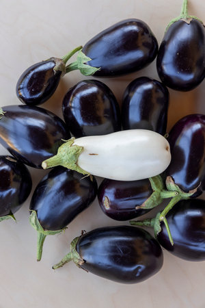 A bunch of eggplants, some of which are black and some are white. There is one white eggplant in the middle of the bunch, surrounded by the black onesの写真素材