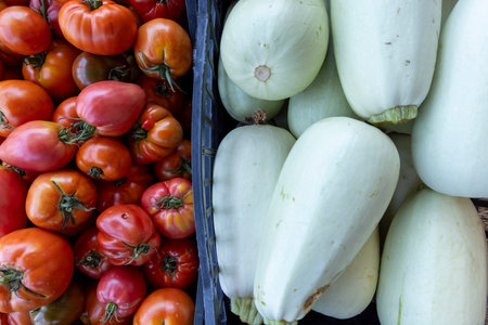 A basket of white squash sits next to a basket of red tomatoes. The squash is sliced and ready to be eatenの写真素材