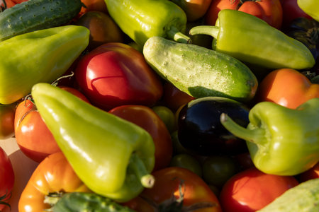 A bunch of vegetables including tomatoes, cucumbers, and peppers. The peppers are green and red, and...