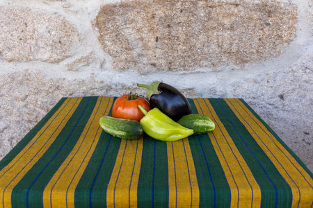 A variety of vegetables, including tomatoes, peppers, and cucumbers, are arranged on a green and yellow tableclothの写真素材