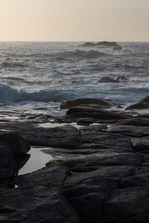 The ocean is calm and the sky is a beautiful shade of blue. The rocks on the shore are large and...