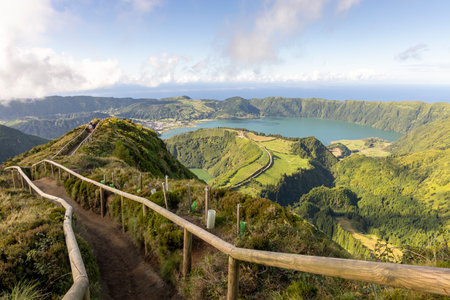 A scenic view of a lake and mountains with a wooden fence leading to the top at Sete Cidades, Azores. The view is peaceful and serene, with the mountains in the background and the lake in the foregroundの写真素材