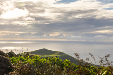 A beautiful view of the ocean with a hill in the background at Sete Cidades, Azores. The sky is cloudy and the sun is shining through the cloudsの写真素材