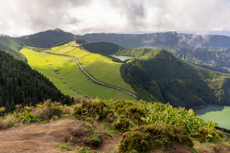 A mountain range with a green hillside and a lake in the distance at Sete Cidades, Azores. The sky is cloudy and the landscape is peacefulの写真素材