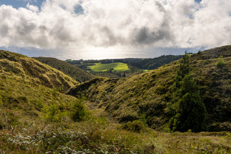 A beautiful landscape with a mountain range and a body of water at Sete Cidades, Azores. The sky is cloudy, and the sun is shining through the clouds. The scene is peaceful and serene, with the treesの写真素材