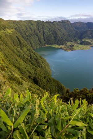 A mountain range with a lake in the foreground. The lake is surrounded by lush green trees and the mountains are covered in trees at Sete Cidades, Azores.の写真素材