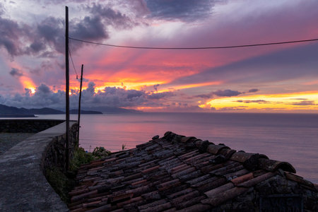 A beautiful sunset over the ocean with a wire running across the sky. The sky is filled with clouds and the sun is setting in Sao Miguel, Azoresの写真素材