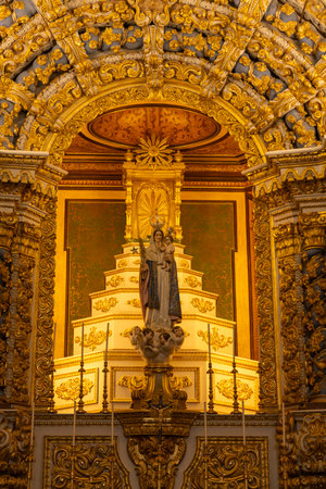 A gold and white church with a statue of a woman and a child. The statue is surrounded by lights and is lit up. In Sao Miguel, Azores.の写真素材