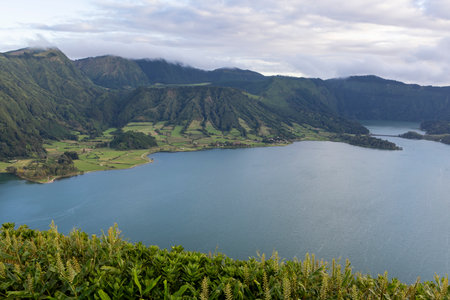 A beautiful lake with mountains in the background at Sete Cidades, Azores. The water is calm and clear. The mountains are covered in trees and the lake is surrounded by green hills.の写真素材