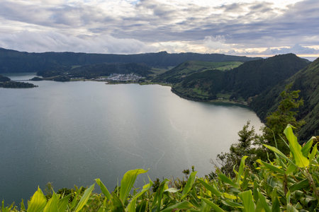 A beautiful lake with a green hill in the background at Sete Cidades, Azores. The lake is calm and peaceful. The sky is cloudy, but the sun is still shining through the clouds.の写真素材