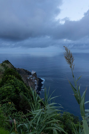 A beautiful view of a small town with a lighthouse and a rocky shoreline. The sky is cloudy and the water is calmの写真素材