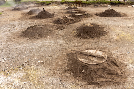 A bunch of caldeira holes for geothermal cooking with a large metal object in the middle. The dirt is piled up in a circle around the object at Furnas, Azoresの写真素材