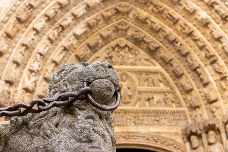 A stone statue with a chain around its neck is in front of a building. The chain is rusty and the statue appears to be chained to a stone pillar. The building is oldの写真素材