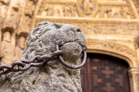 A large stone lion is chained to a pillar with a chain. The lion is positioned in front of a building, with the chain visible from the doorway. The scene gives off a sense of imprisonmentの写真素材
