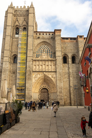 Avila, Spain, December 10, 2025: A group of people are walking down a street in front of a large building. The building has a yellow scaffolding on it.のeditorial素材
