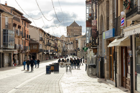 Toro, Spain, December 10, 2025: A busy street with people walking and sitting outside of cafes. The street is lined with shops and buildings, and there is a large church in the background.のeditorial素材