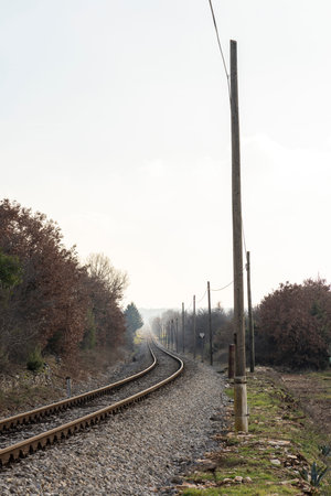 A train track with a pole in the middle of it. The pole is bare and has no wires on it. The sky is...