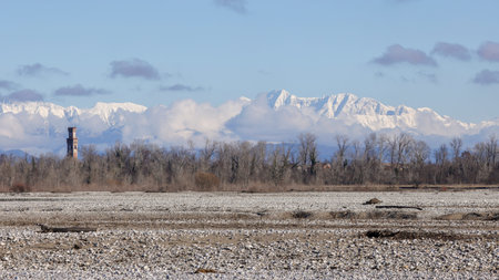 Winter landscape showing snow covered mountains, a dry riverbed, and distant bare trees