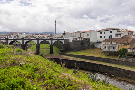 Ribeira Grande, Azores, Portugal, October 8, 2025: A bridge spans a river in a town with houses on both sides. The bridge is old and has a rustic appearance. The town is quiet and peaceful.のeditorial素材