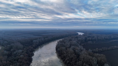 Tisza river winding through a vast bare forest under a cloudy sky, tiszaroff, hungary