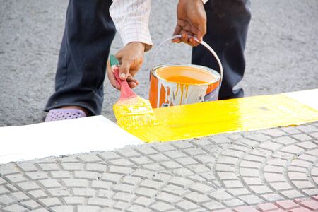 The hand of a man painting footpath  with yellow and white paint の写真素材