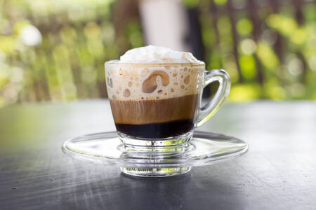 Hot espresso coffee with white cream on table.