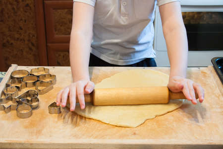 The boy rolls the dough with a rolling pin for homemade biscuits