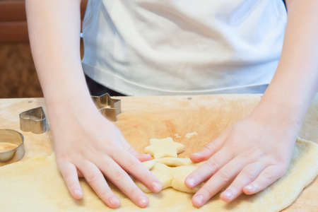 The boy carves figures out of dough for biscuits