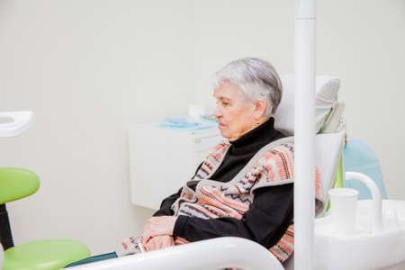 An elderly woman is sitting in a chair at a dentist's receptionの写真素材