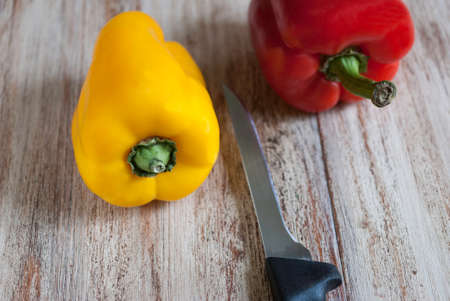 red and yellow peppers with a kitchen knife lying on the table surfaceの写真素材