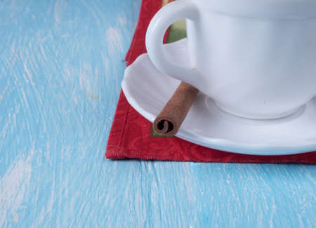 White Cup on a saucer with a cinnamon stick standing on a red napkin.の写真素材
