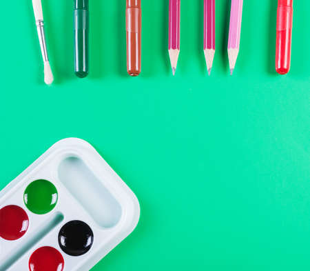 Watercolor paints and pencils on a green background. top viewの写真素材