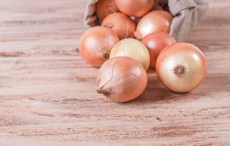 Bag with spilling onions on a wooden backgroundの写真素材
