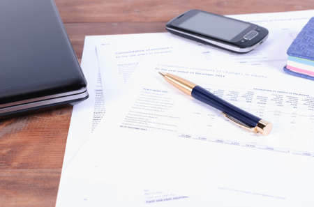 Pen, laptop and mobile phone lying on tax and financial documentsの写真素材