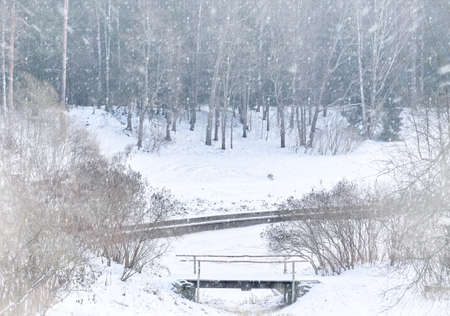 Snowfall and fog on a winter day on the river. Winter landscape with a wooden bridgeの写真素材