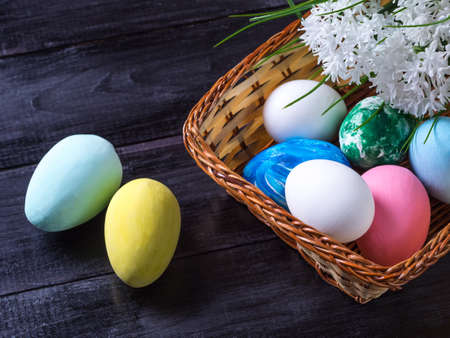 Basket with Easter eggs, white flowers and lying next to a basket of eggs on a dark wooden...