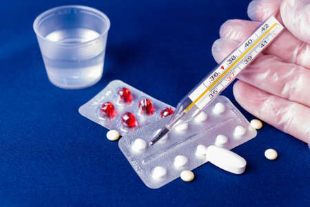 A gloved hand with a thermometer on a tablets background