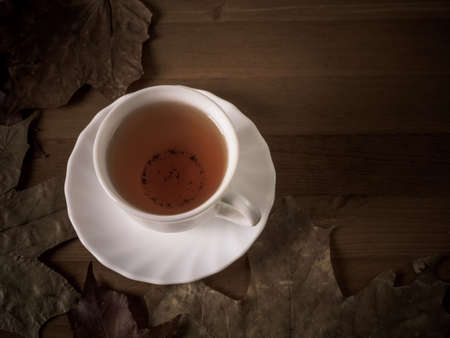 Cup of hot tea on a wooden table surrounded by autumn leaves.の写真素材