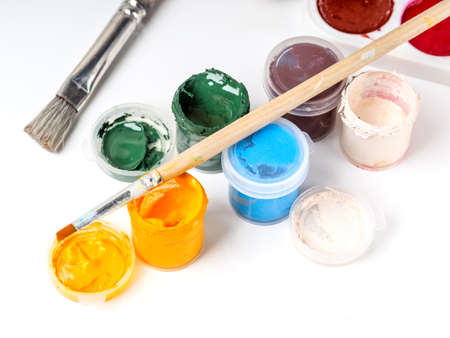 Jars with gouache and paint brushes on a white background