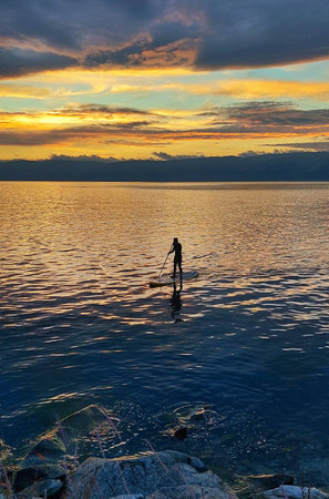 A lone swimmer on a swimming board,a sunset,golden highlights on the water.Male silhouette against the sunset.Sports equipment.の写真素材
