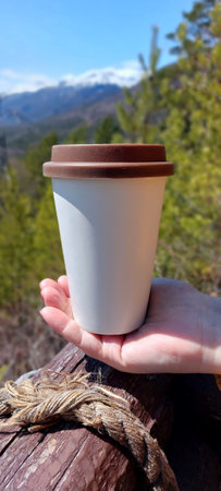 Paper cup of coffee in female hand on the background of the mountainsの写真素材