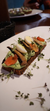 Sandwiches with avocado, tomato, smoked sprat and chicken egg on a white plateの写真素材